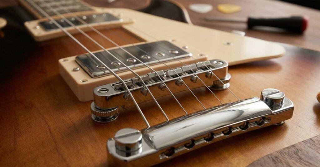 Close-up detalhado em ângulo de uma ponte fixa Tune-o-Matic cromada com sistema Stopbar Tailpiece em uma guitarra sunburst estilo Gibson.